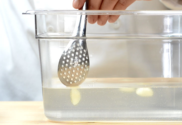 Spherification: Tomato water spheres in alginate bath, perforated spoon